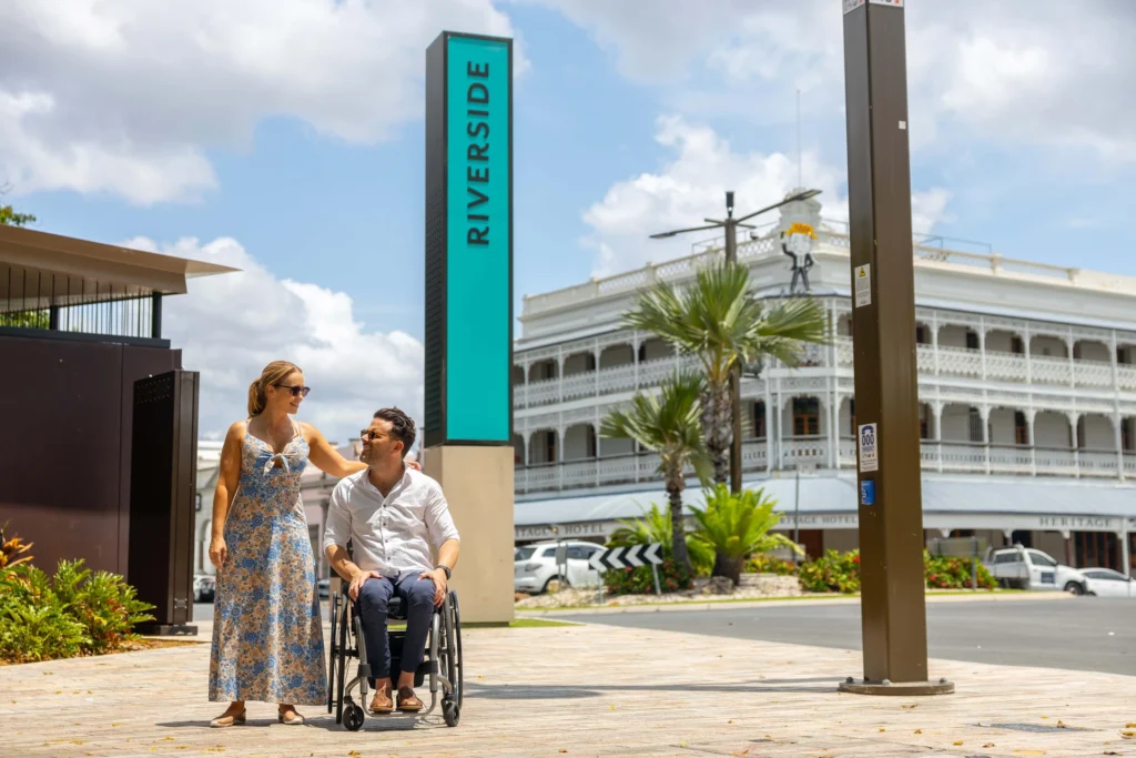 A woman and a man in a wheelchair are outside near a sign that reads 