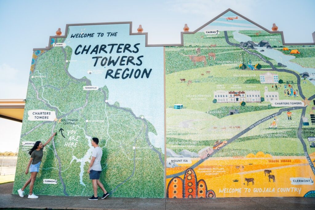 Two people point at a large outdoor map mural marked 