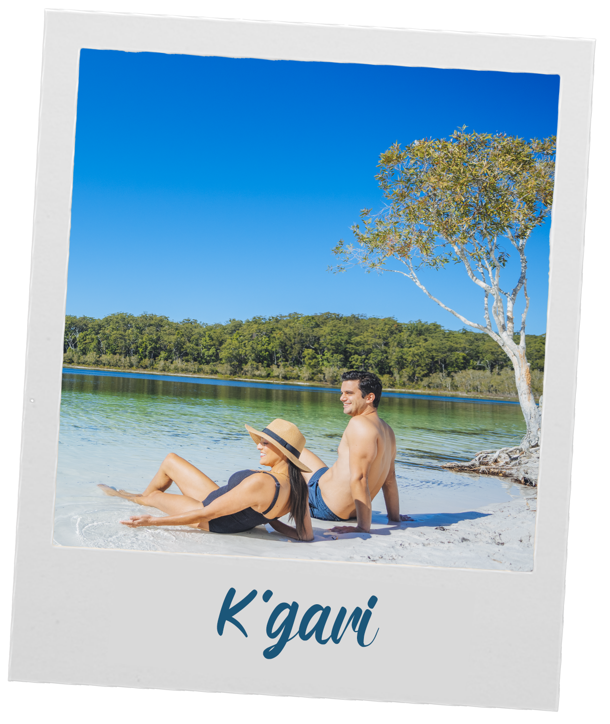 Two people relax on a sandy shore by clear water, with a tree and forest in the background, under a clear blue sky. The word 