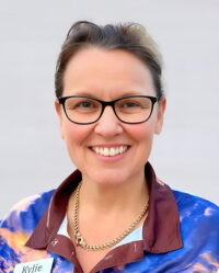 A person wearing glasses and a patterned shirt with a name tag that reads 