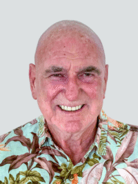 A smiling older man with a bald head wears a floral-patterned shirt against a plain light gray background.