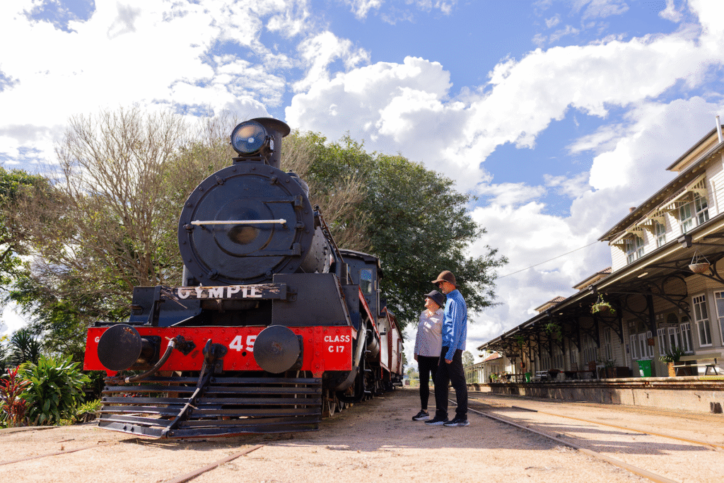 Two people stand near the front of a black steam locomotive labeled 