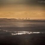 City skyline in the distance with layered hills and misty landscape in the foreground under a golden sky.