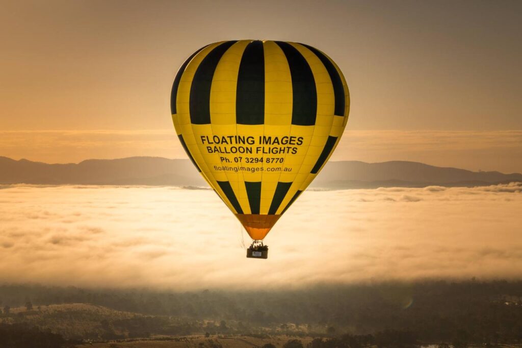 A yellow and black hot air balloon with "Floating Images Balloon Flights" text floats above a foggy landscape at sunrise.