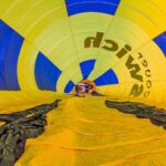 View from inside an inflated yellow and blue hot air balloon lying on the ground, with the basket visible at the far end.