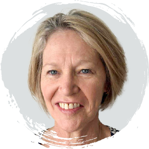 Middle-aged woman with short, light blonde hair, smiling at the camera against a light grey background with a white circular border.
