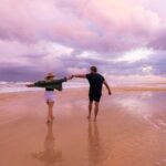A man and woman holding hands on a beach.