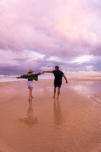 A man and woman holding hands on a beach.