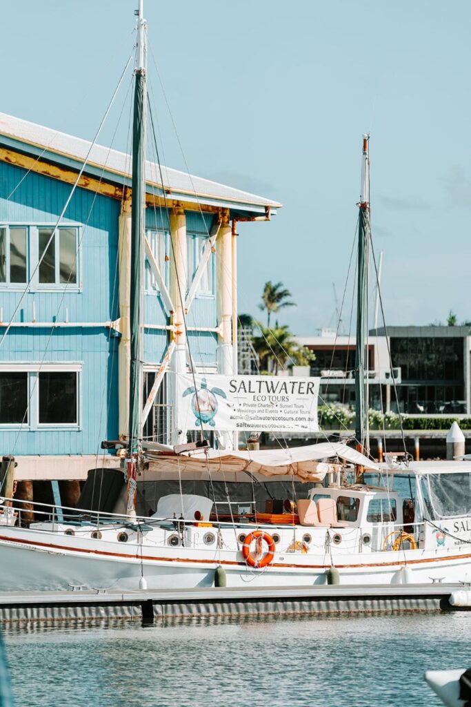 A white sailboat docked near a blue building displays a "Saltwater Eco Tours" banner on its side.