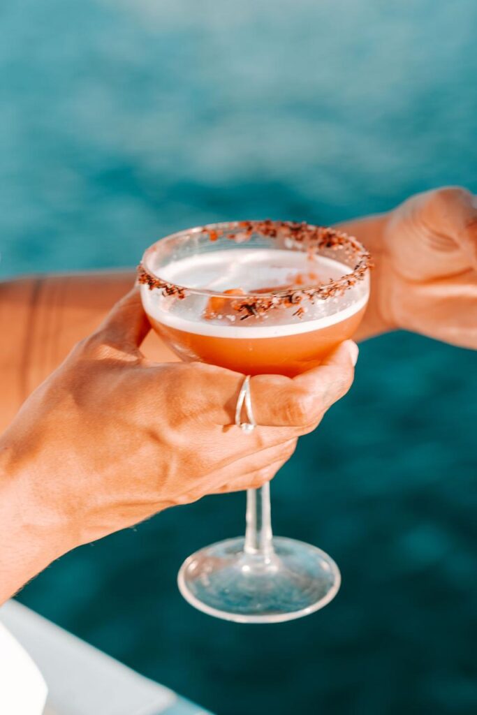 A person holding a cocktail in a coupe glass with a chocolate-rimmed edge, against a blurred blue background.