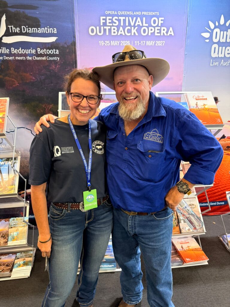 Two smiling people pose together at a booth for the Festival of Outback Opera, with brochures and promotional banners in the background.