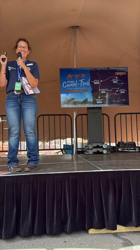 A woman stands on an outdoor stage holding a microphone, with a map labeled 