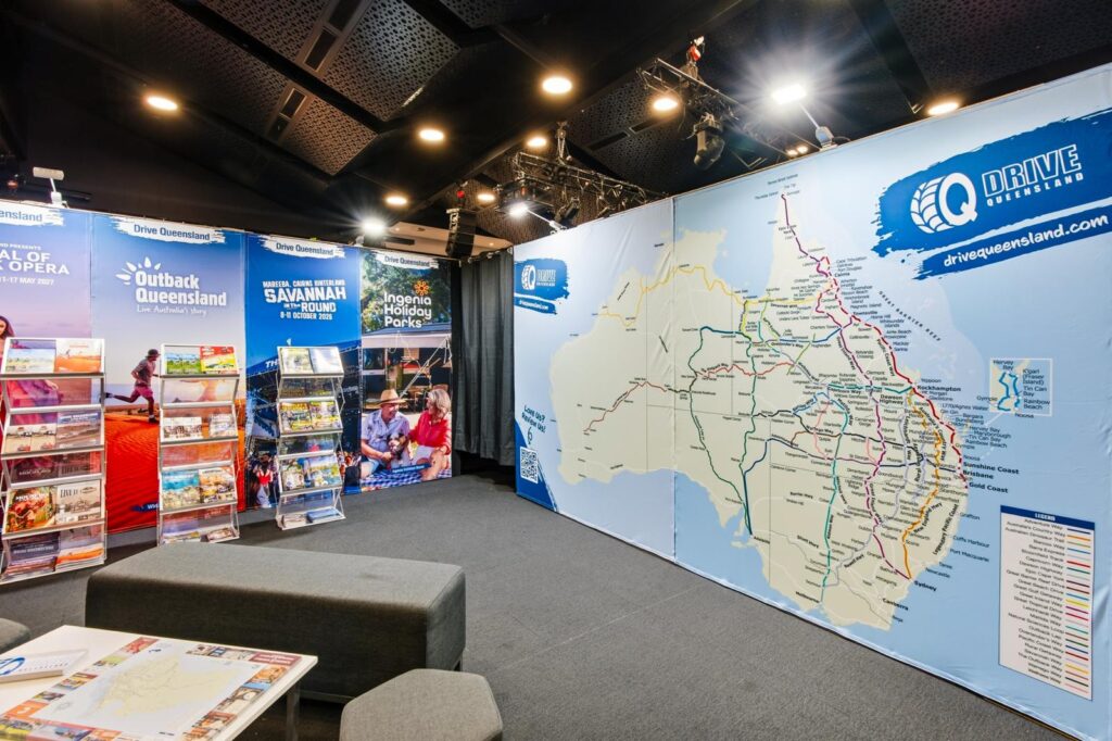 Tourist information booth with brochures, posters, and a large map of Australia displaying routes and attractions under bright indoor lighting.