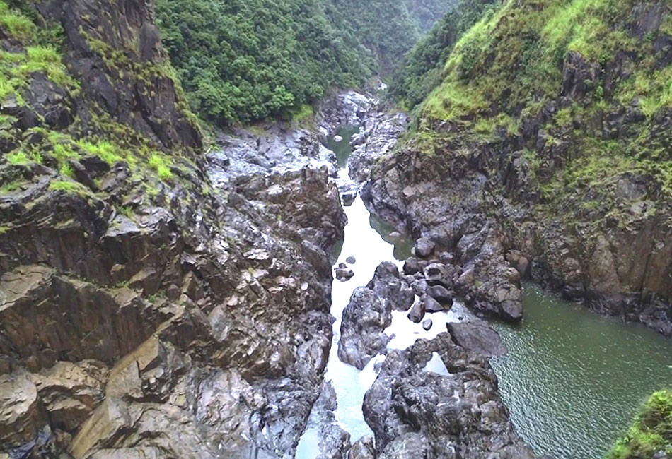 Rocky river gorge with steep, green-clad cliffs and patches of water flowing between large rugged rocks.