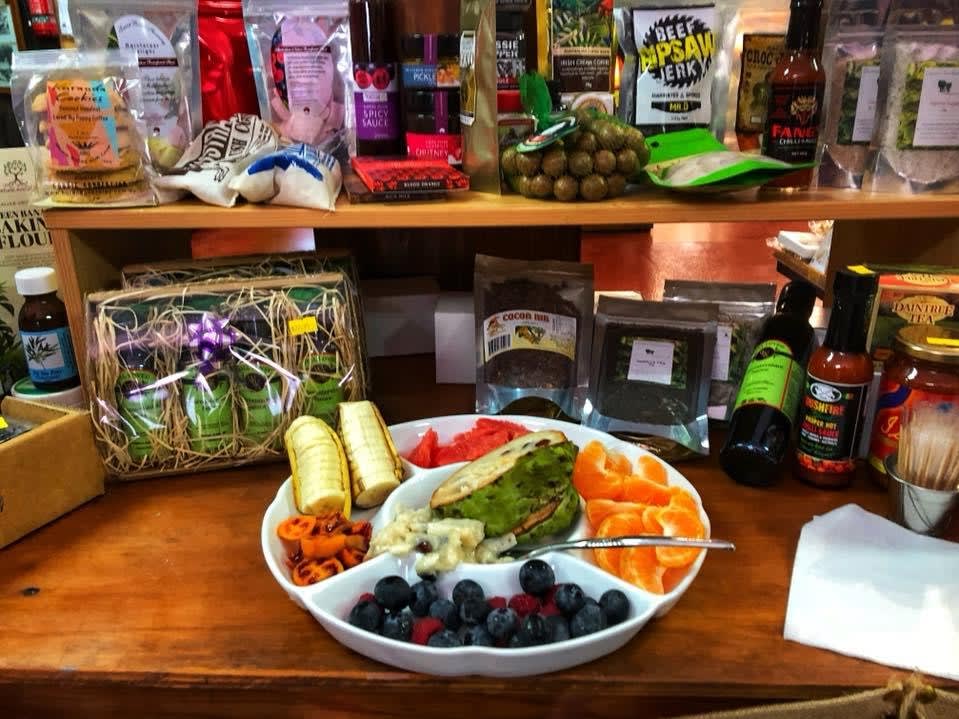 A plate of assorted fruits and vegetables sits on a counter surrounded by packaged food items, gift baskets, and condiments on shelves in a store.