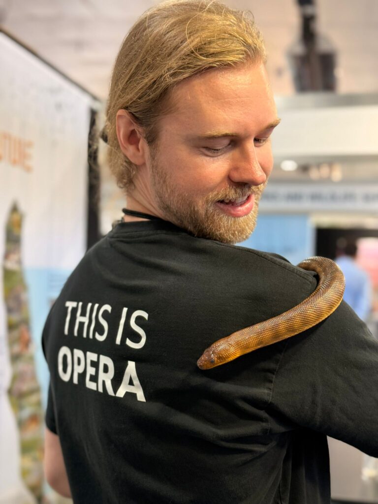 A man with blonde hair and a beard, wearing a black shirt that says 