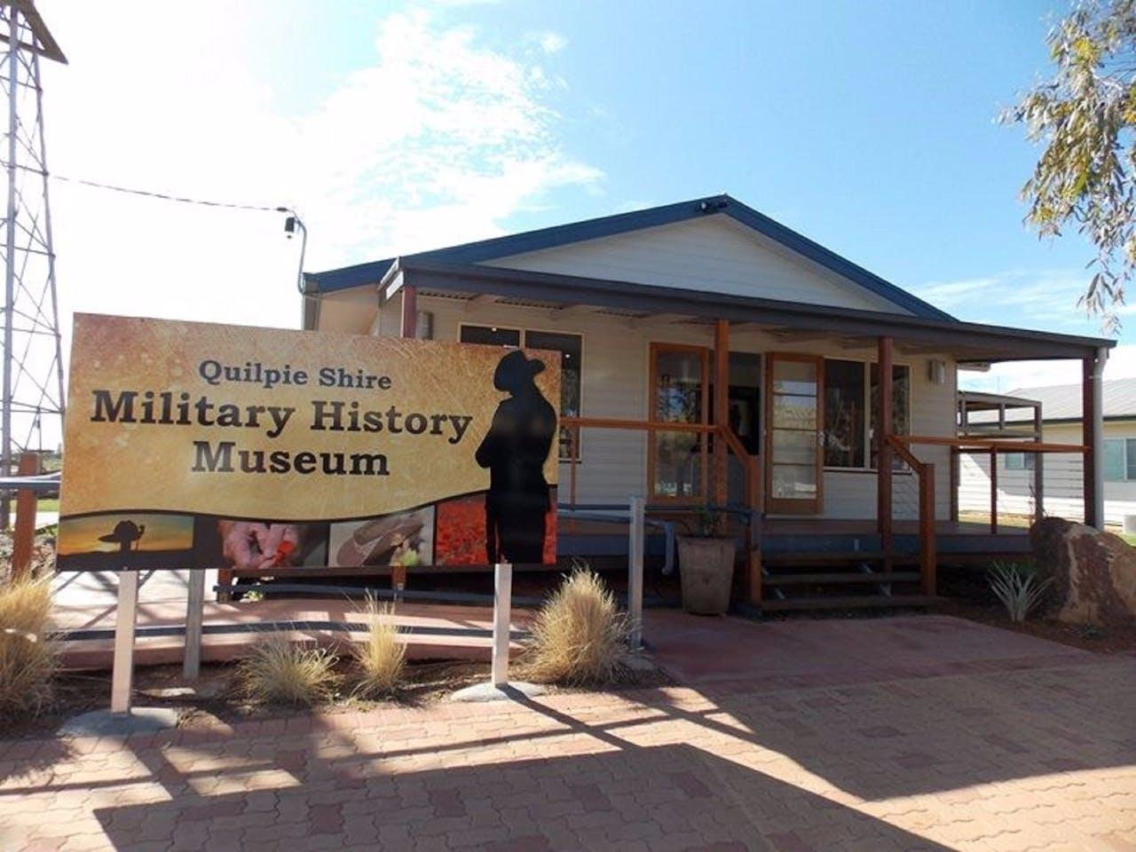 A small building with a sign in front reading "Quilpie Shire Military History Museum" under a clear blue sky.